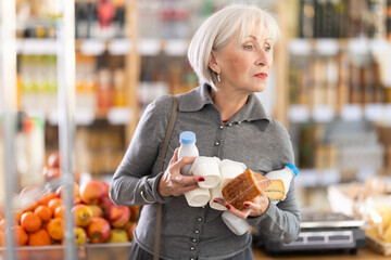 Elderly woman buyer chooses fresh dairy products in grocery store