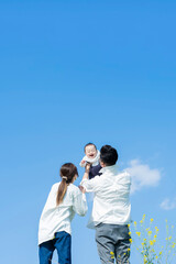 青空のもと、赤ちゃんを高く抱き上げる父母