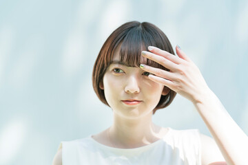Fototapeta premium 髪を整える女性と、白壁に映る木々の影
