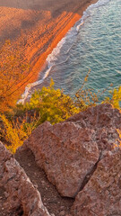 Aerial view of sandy beach with turquoise waves framed by rocky cliffs and coastal vegetation at sunset.
