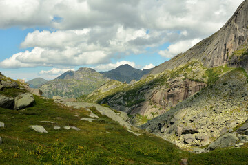 A deep crevice between two mountain ranges with rocky slopes on a cloudy summer day.