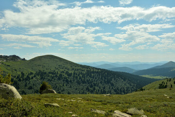 Fototapeta premium A small clearing with a scattering of small stones on the flat top of a mountain in a chain of pointed rocks on a sunny summer day.