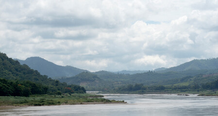 Winding river surrounded by lush green mountains under a cloudy sky, atmosphere natural scene.