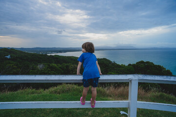 Child standing on fence looking over bay