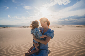 Mum holding toddler on sand dune at sunset