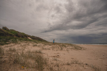 Boy on top of sand dune in from of stormy sky