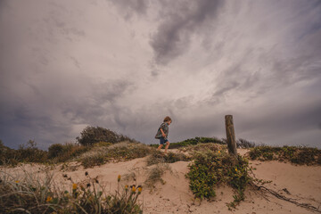 Boy exploring top of sand dune dramatic sky