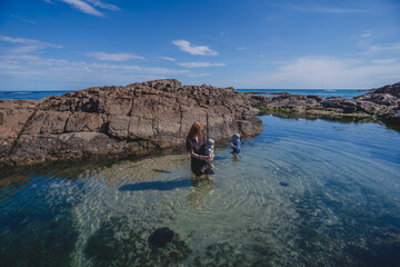 Mum holding baby exploring rock pool