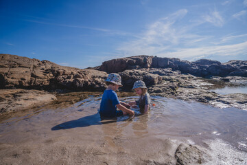 Two children playing in rock pool with hats on