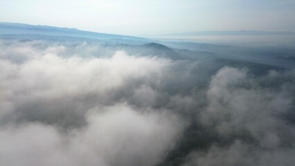 Dramatic Aerial drone view of hills with lush green trees with morning mist above with a background of rows of mountains