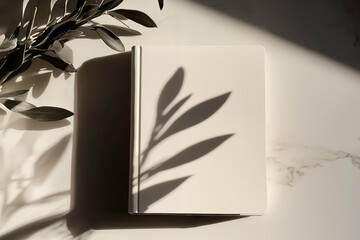 Photo of a minimalist blank journal on an elegant white table with sun rays and shadows. Top View of personal planner  Mockup paper notebook design.
