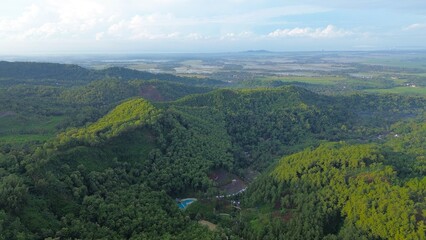 Dramatic Aerial drone view of hills with lush green trees with morning mist above with a background of rows of mountains