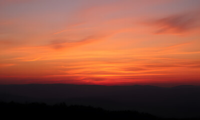Naklejka premium Orange sunset sky with distant mountain silhouettes. Perfect for nature-themed designs, travel brochures, outdoor adventure promotions, or inspirational content