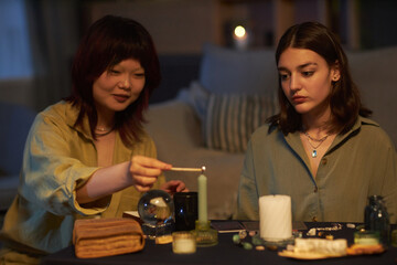 Ethnically diverse female friends sitting at coffee table with magical objects on it, lighting up...