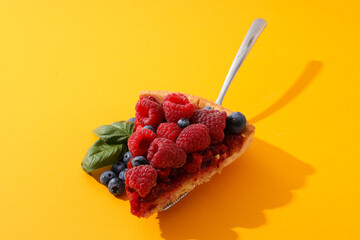 Piece of berry pie and basil leaves on yellow background, close up