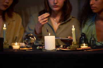 Medium closeup of three diverse female friends practicing divination, while sitting at coffee table with candles and magical objects on it