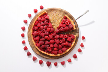 Berry pie on wooden plate and raspberries on white background, top view
