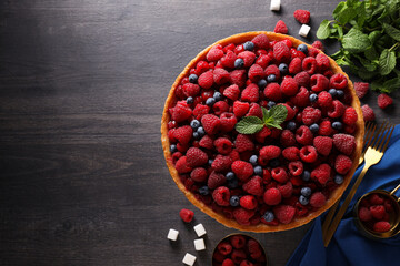 Berry pie, mint and cutlery on towel on wooden background, space for text