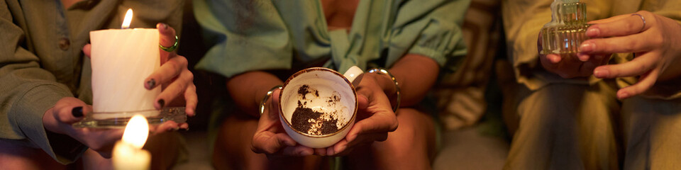 Group of three diverse girls reading coffee grounds, predicting future during magic-themed party at...