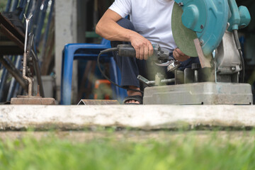 A worker grinding a coffee portafilter with a handheld grinder next to a large industrial cutting machine in a Thai workshop.