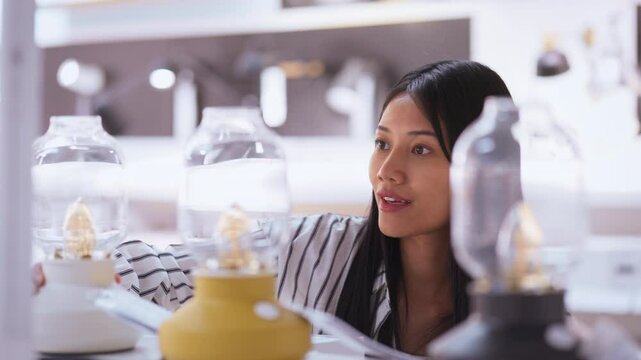 Confident young woman browsing stylish lamps in a furniture store, carefully selecting modern lighting for home decor and interior design to enhance her living space