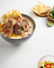 Enjoy a nourishing stew featuring tender meat, crispy bread, fresh limes, and vibrant diced tomatoes, perfect for sharing at lunch or dinner