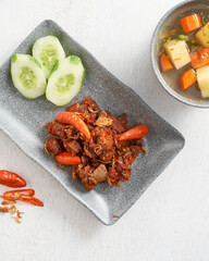 Spicy beef topped with fresh chilies is accompanied by cucumber slices and a warm vegetable soup,...
