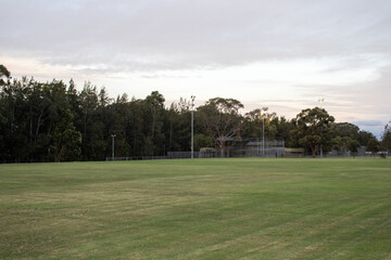 Captivating photo of a cricket ground in International Peace Park, Western Sydney, Australia. Stunning sunset glow through clouds, with lush greenery and trees in the background.