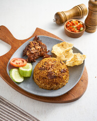 Delicious rice cooked with spices, accompanied by tender meat, cucumber, tomato, and crispy snacks, served on a rustic wooden plate