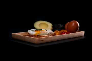 Vegetarian breakfast, fried egg, avocado, tomato on black background