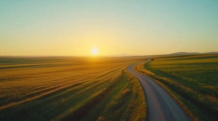 A winding road through golden fields at sunset, leading into the distance with a clear sky