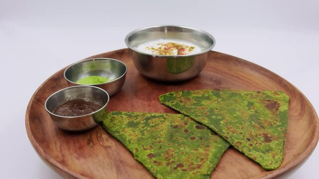 Paratha on wooden platter with yogurt and chutney