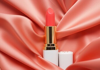 Luxury lipstick in coral pink shade with gold and white packaging on soft silky background in studio lighting