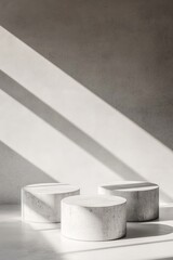 Three cylindrical white marble podiums in sunlight against a grey wall.