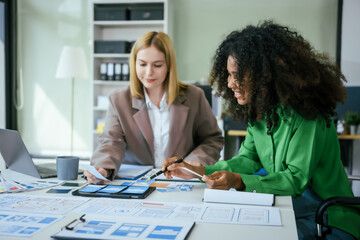 An African American businesswoman and a Caucasian woman collaborate at a desk, brainstorming...