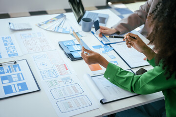 An African American businesswoman and a Caucasian woman collaborate at a desk, brainstorming...