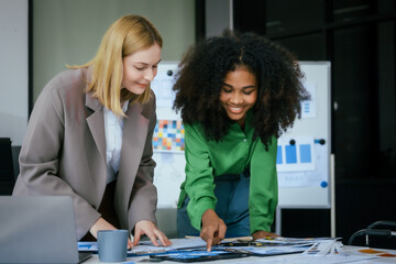An African American businesswoman and a Caucasian woman collaborate at a desk, brainstorming...