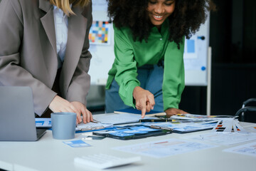 An African American businesswoman and a Caucasian woman collaborate at a desk, brainstorming...