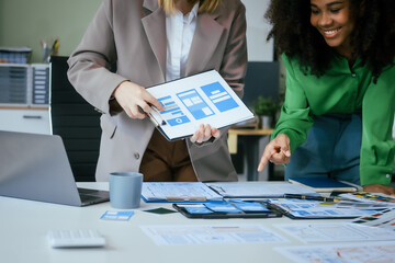 An African American businesswoman and a Caucasian woman collaborate at a desk, brainstorming...