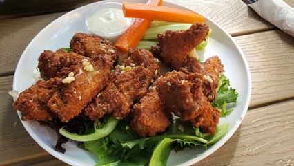 Crispy fried chicken wings served with vegetables and dipping on a white round plate