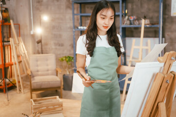 A happy Asian teenage girl painting with a brush on canvas at home, enjoying creativity and relaxation in a cozy, peaceful setting filled with artistic inspiration and vibrant colors