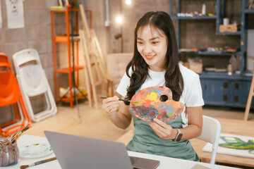 A happy Asian teenage girl painting with a brush on canvas at home, enjoying creativity and relaxation in a cozy, peaceful setting filled with artistic inspiration and vibrant colors