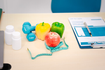 A nutritionist's table with a vegetable basket, fruits, pill bottles, and a dumbbell, symbolizing...