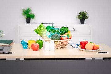 A nutritionist's table with a vegetable basket, fruits, pill bottles, and a dumbbell, symbolizing...