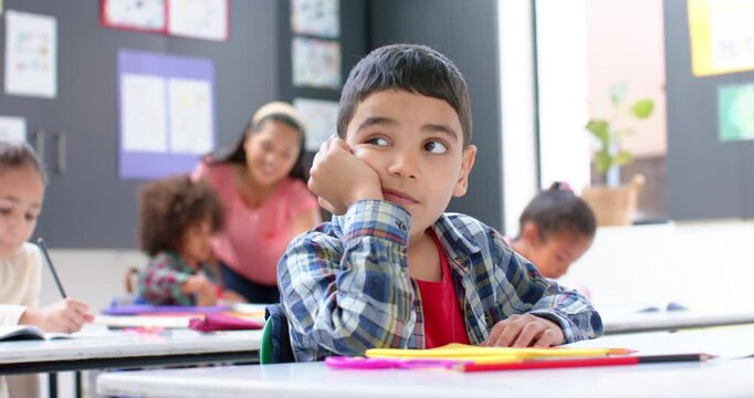 In school, boy daydreaming at desk while classmates and teacher working