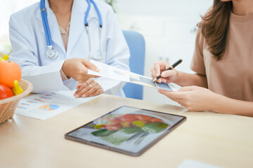 A young female nutritionist expert talks to a female patient at a table, recommending a healthy diet with vegetables and fruits to promote wellness, balanced nutrition, and effective weight loss