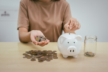 A young woman saves money for the future by putting coins in a piggy bank on the table, managing...