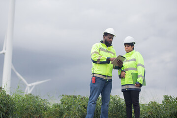 Two engineer check and examining wind turbines in wind farm, renewable energy and teamwork in a...