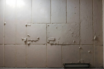 Wall of white tiles with partially destroyed surface and rough edges.