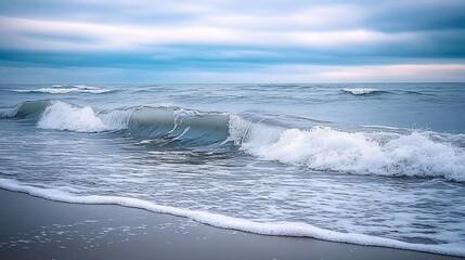 Fototapeta premium Ocean waves rolling onto the sandy beach under a cloudy sky with soft light and calm mood